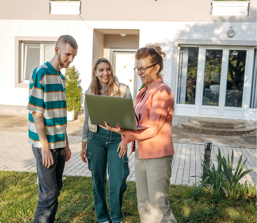 Three people looking at a laptop outdoors.