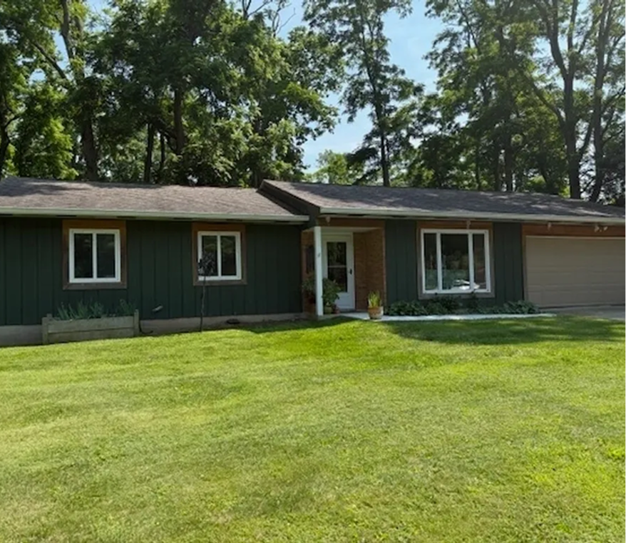 Green house with lawn and surrounding trees.