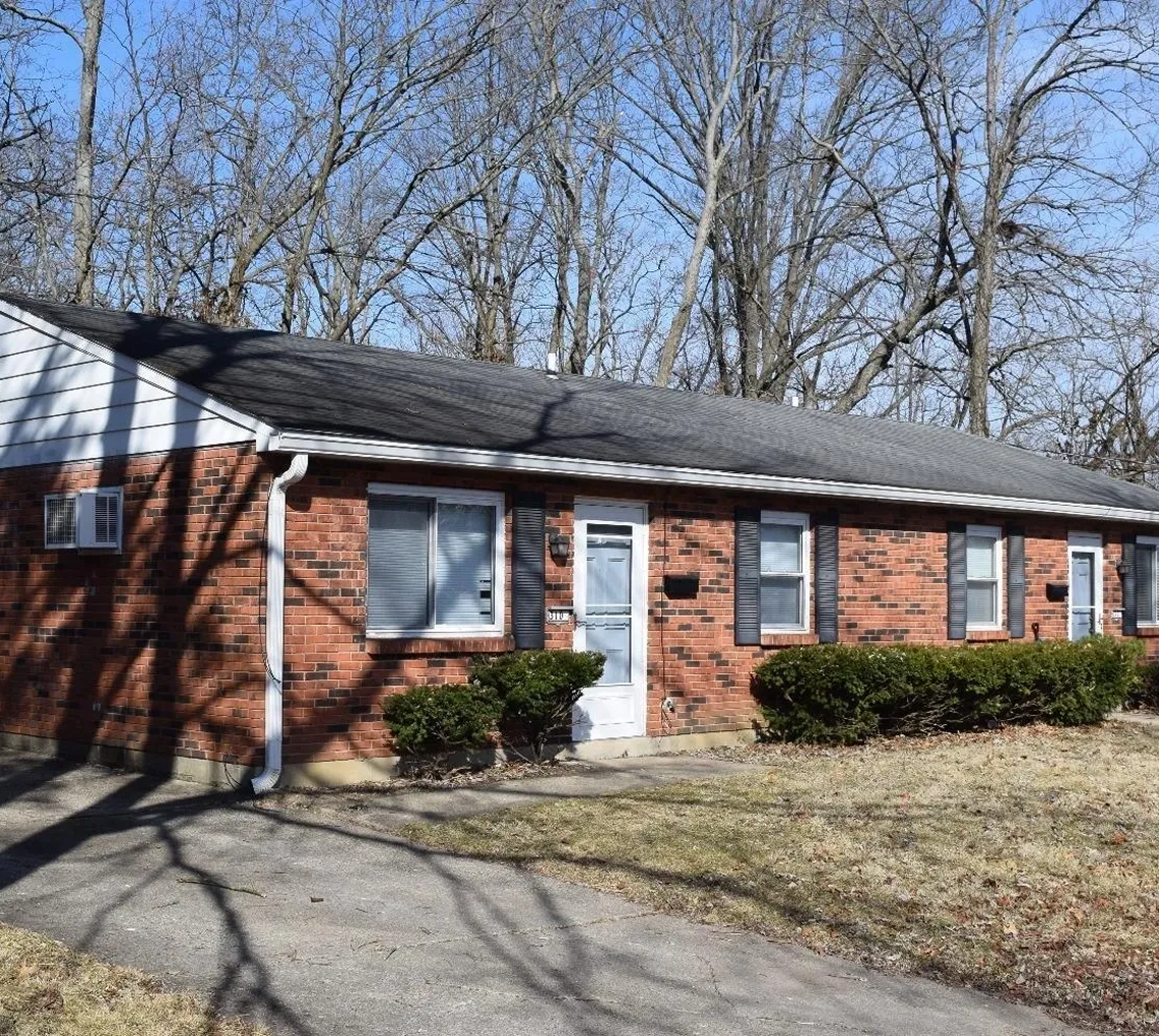 Red brick house with white trim, trees.